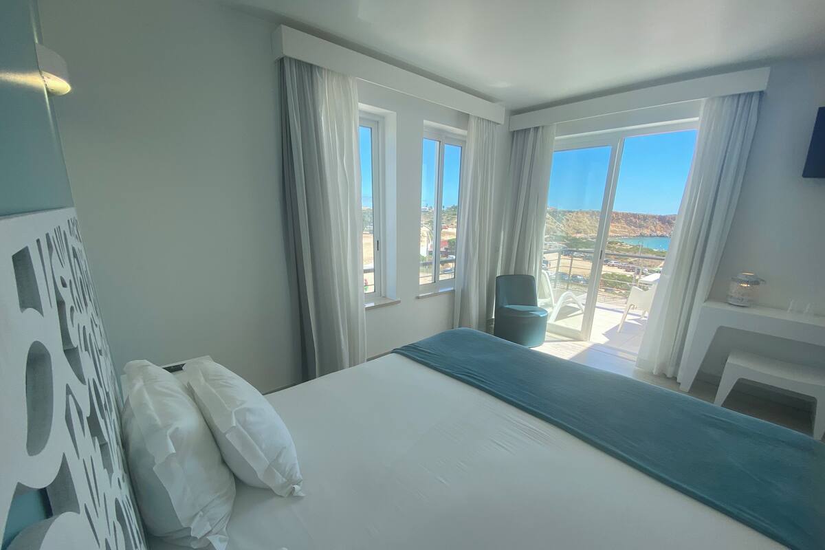 Een hotelkamer met een bed, een stoel, een bureau en uitzicht op het landschap.
