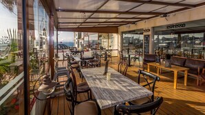 Un espace de restauration en plein air avec des tables et des chaises en bois, une vue sur la ville grâce à de grandes fenêtres et un bar à espresso.