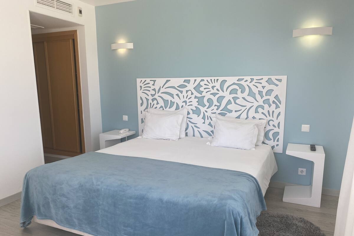 Een slaapkamer met een bed, nachtkastjes, een telefoon en een decoratief hoofdeinde.