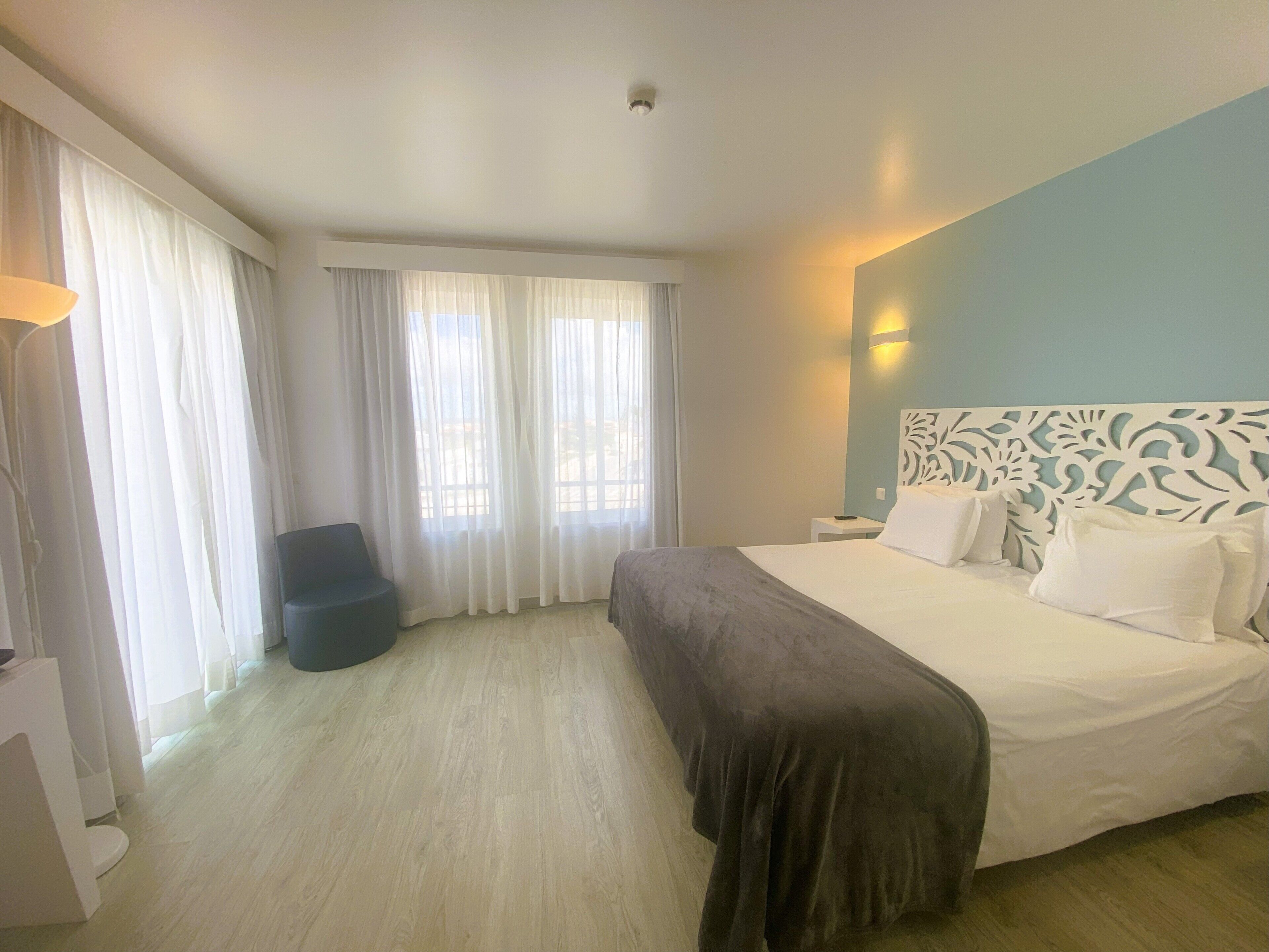 Una habitación de hotel con una cama, una silla, una mesita de noche y una ventana con cortinas.
