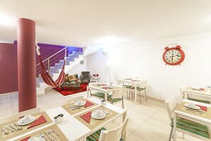 Ein Essbereich mit gedeckten Tischen, eine rote Weckeruhr an der Wand und eine Treppe im Hintergrund.