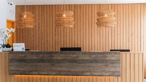Un comptoir d’accueil avec un panneau en bois en arrière-plan, trois suspensions en osier et un panneau indiquant qu’il s’agit d’un charmant hôtel-boutique proposant des chambres et le petit-déjeuner.