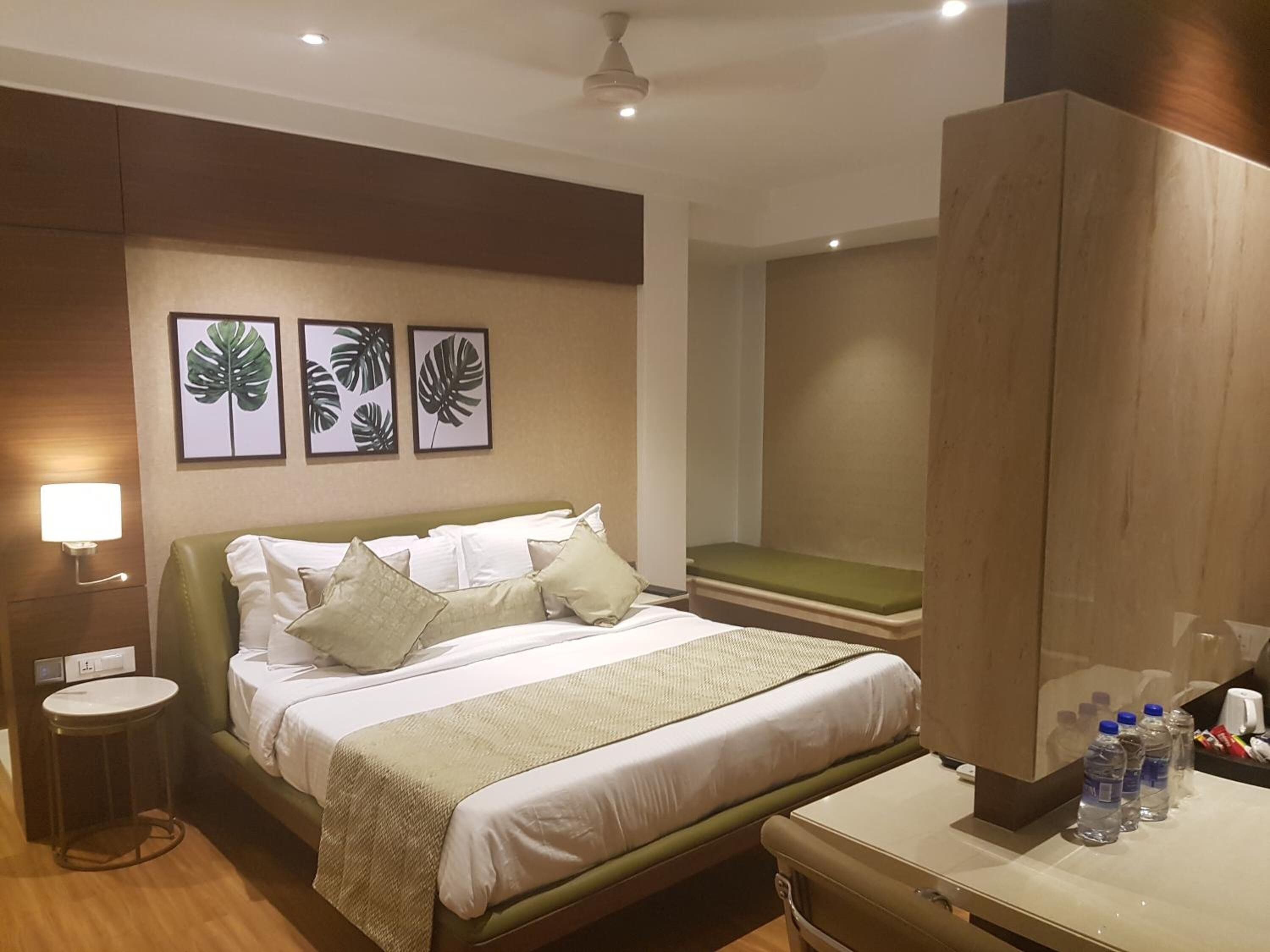 A hotel room with a bed, bedside table, wall-mounted lamp, and framed leaf artwork.