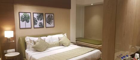 A hotel room with a bed, bedside table, wall-mounted lamp, and framed leaf artwork.