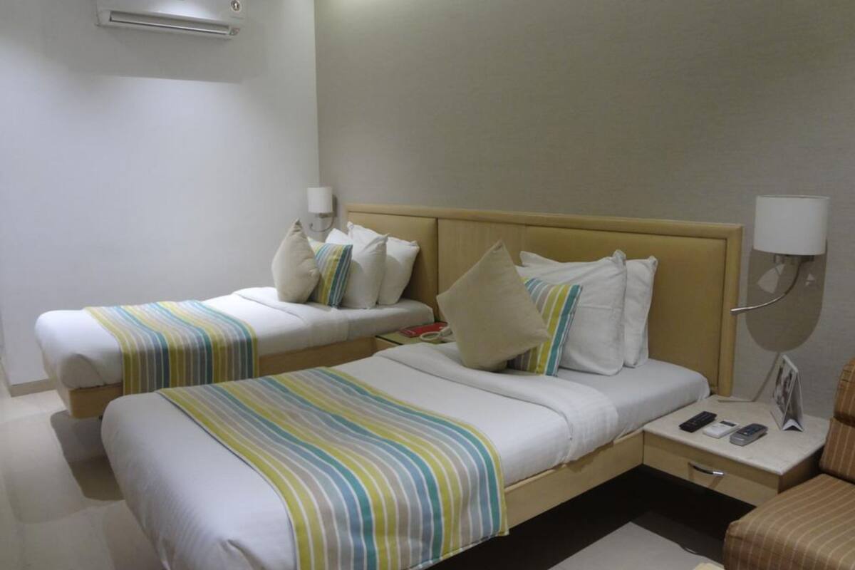 A hotel room with two single beds, a bedside table with a lamp, a chair, and a small table with a phone and a book.