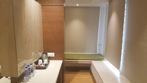 A hotel room with a wooden floor, a white counter with a water dispenser, and a green bench. - Hotel Suncity Apollo (Mumbai)