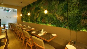 A restaurant with a long table set for dining, a green vertical garden wall, and hanging light fixtures. - Hotel Suncity Apollo (Mumbai)