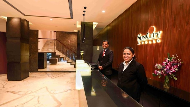 A reception area with a wooden wall, a reception desk, and a staircase in the background. - Hotel Suncity Apollo (Mumbai)