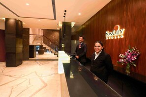 A reception area with a wooden wall, a reception desk, and a staircase in the background. - Hotel Suncity Apollo (Mumbai)