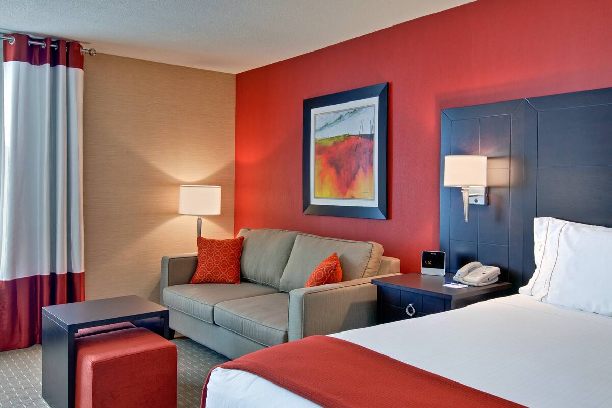 A hotel room with a bed, a sofa, a desk, a phone, and a painting on the wall.
