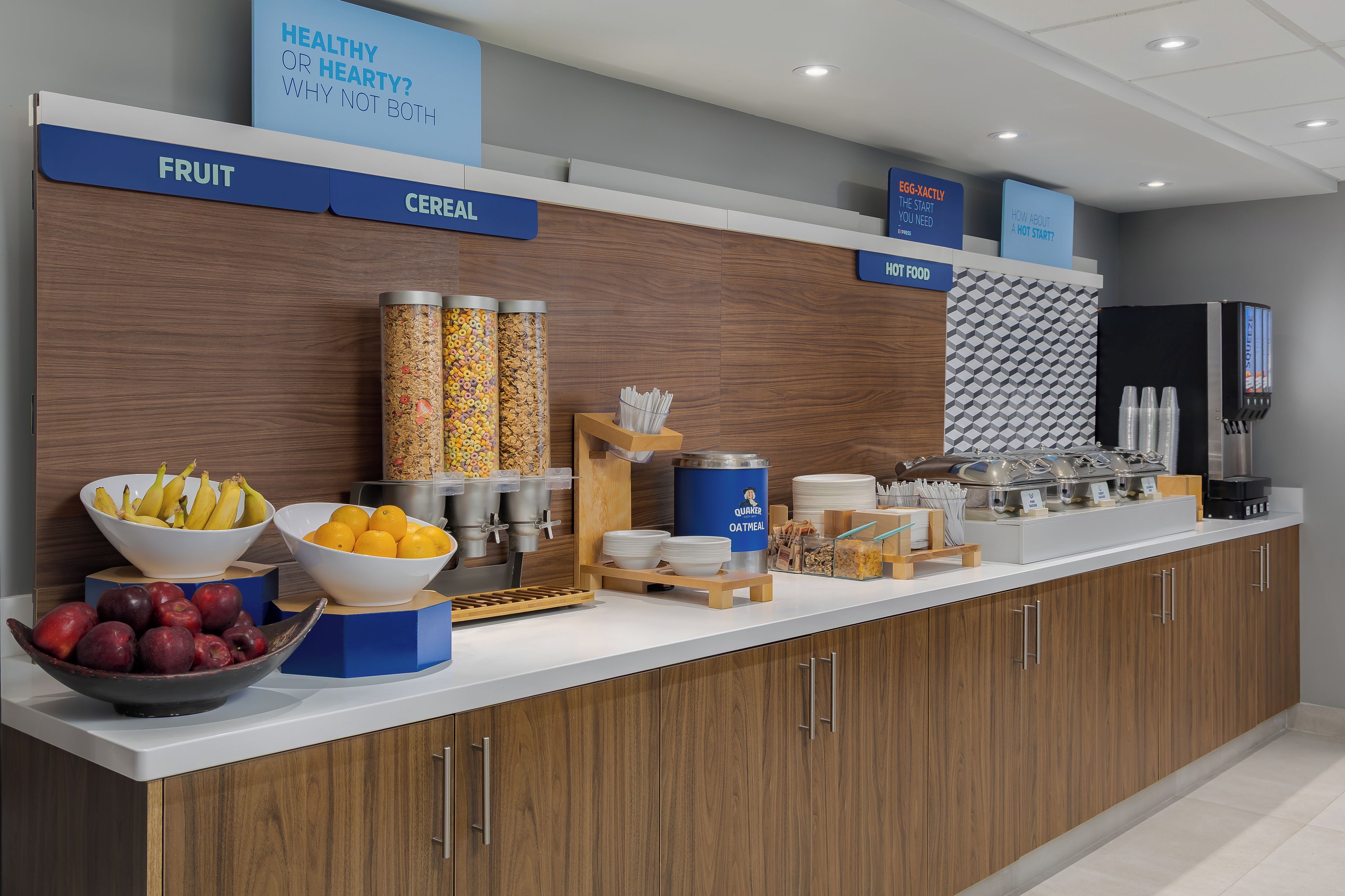 Una barra de desayuno con secciones identificadas para fruta, cereales y huevos, además de diversas opciones de alimentos y una máquina de café.
