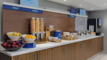 Una barra de desayuno con secciones identificadas para fruta, cereales y huevos, además de diversas opciones de alimentos y una máquina de café.