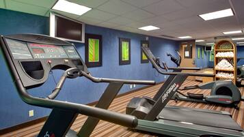 Un gimnasio con equipo de ejercicio, incluyendo cintas de correr y una bicicleta estática, además de una pared decorada con cuadros.