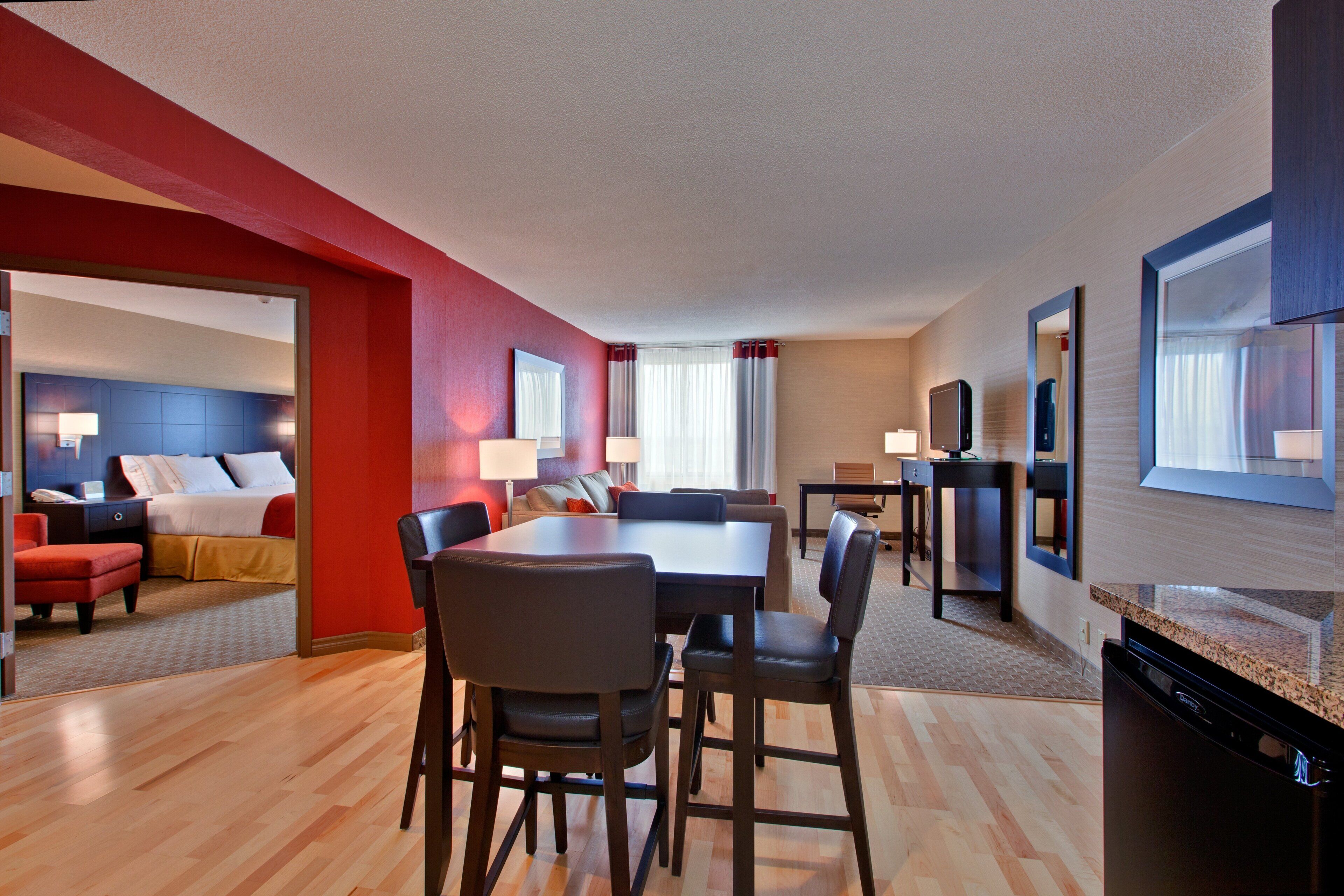 A hotel room with a dining area, a bed, a desk, and a bathroom.
