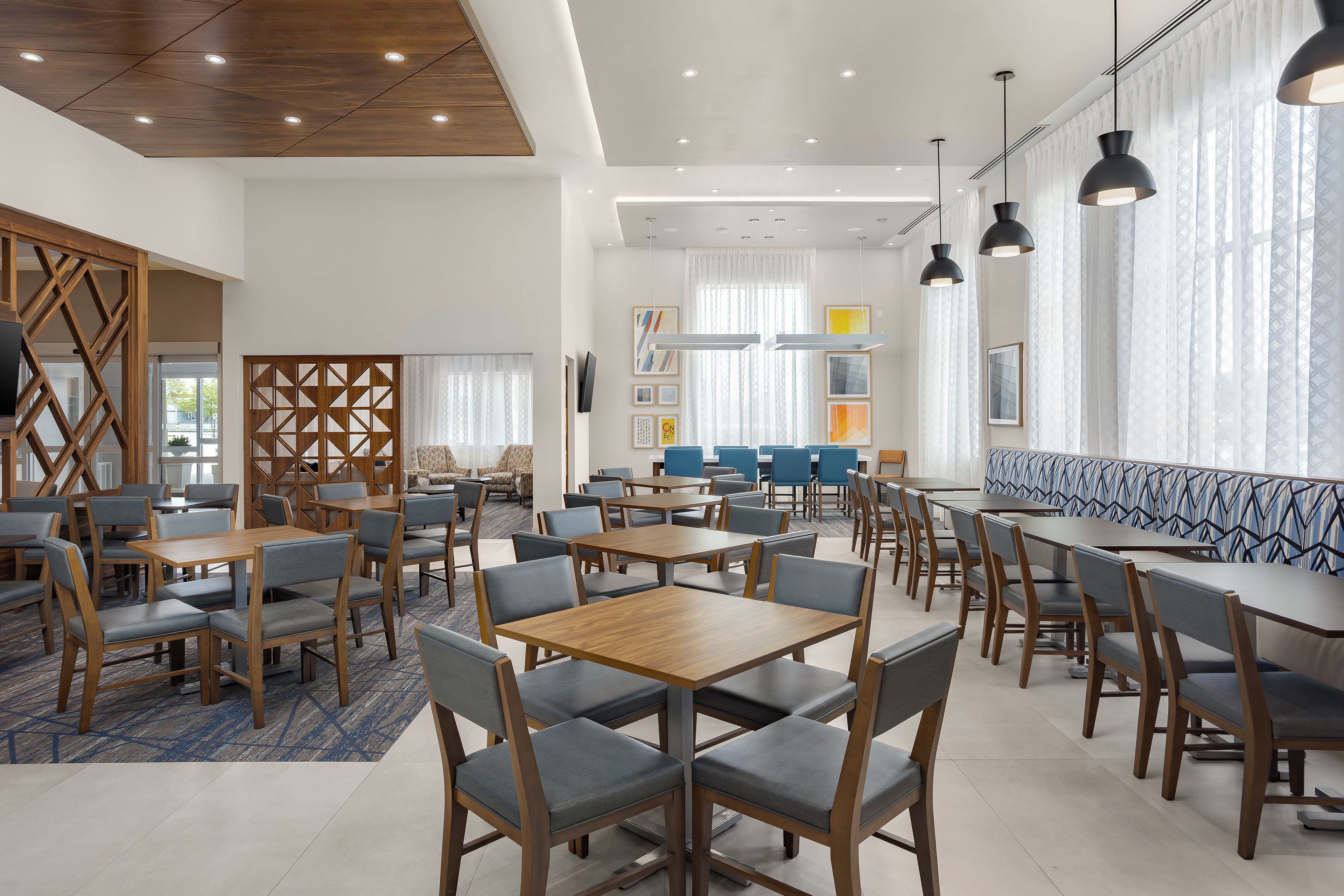 A modern dining area with wooden tables and chairs, a patterned bench, and pendant lighting.