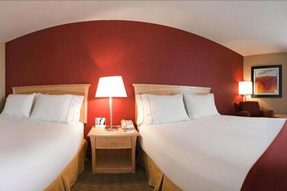A hotel room with two beds, a nightstand with a lamp, and a small table.