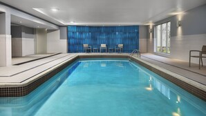 A modern indoor swimming pool with clear blue water, surrounded by a tiled deck and a blue curtain wall. - Holiday Inn Express & Suites Chatham South by IHG (Chatham-Kent)