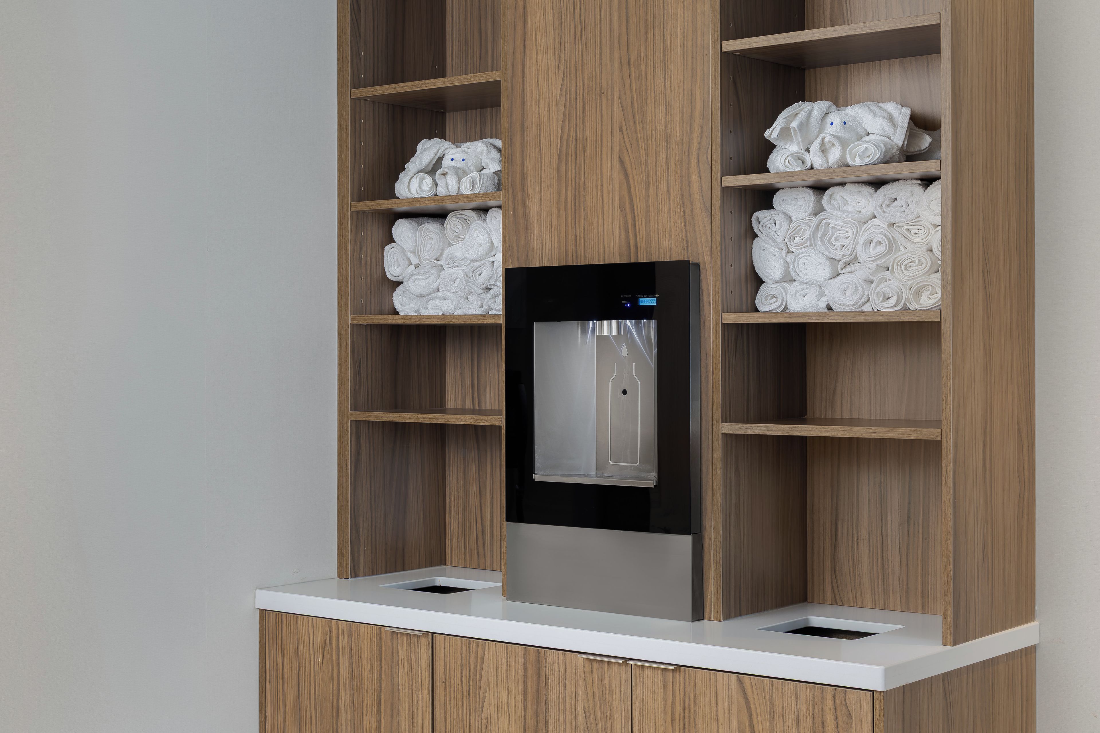 Une salle de bain moderne dotée d’un distributeur d’eau intégré et de serviettes soigneusement pliées, rangées sur des étagères.