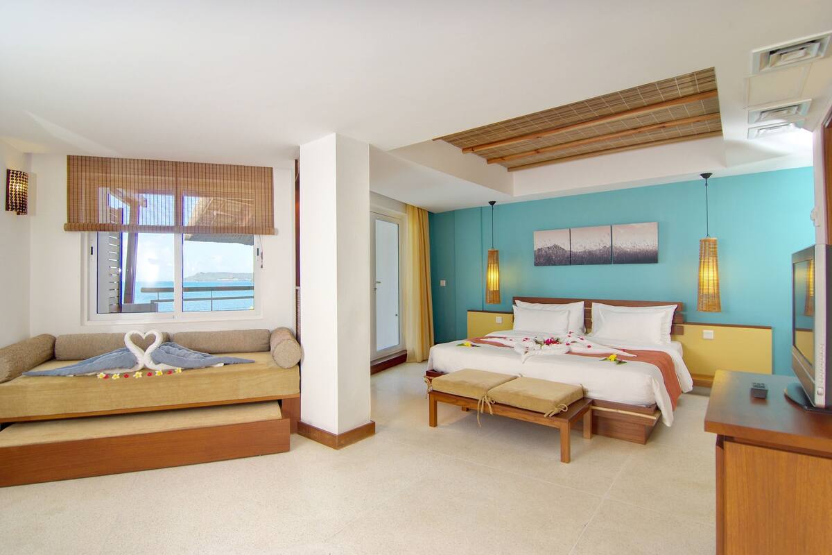 A hotel room with a bed, a sofa, a bench, a TV, and a window with a view.
