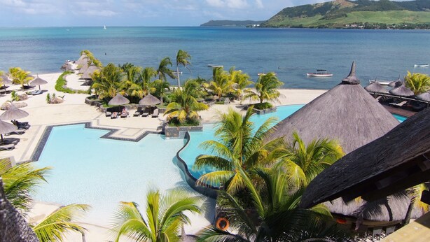 A resort pool area with palm trees, thatched-roof structures, and a view of the sea. - Laguna Beach Hotel & Spa (Grand River South East)
