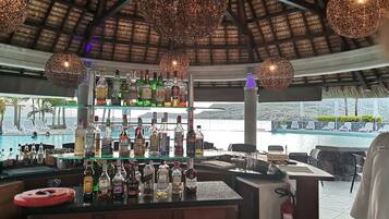 Un bar con diversas botellas de licor, un extintor y vistas a la piscina y la playa.