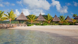 A beach with clear water, palm trees, and thatched-roof huts. - Laguna Beach Hotel & Spa (Grand River South East)