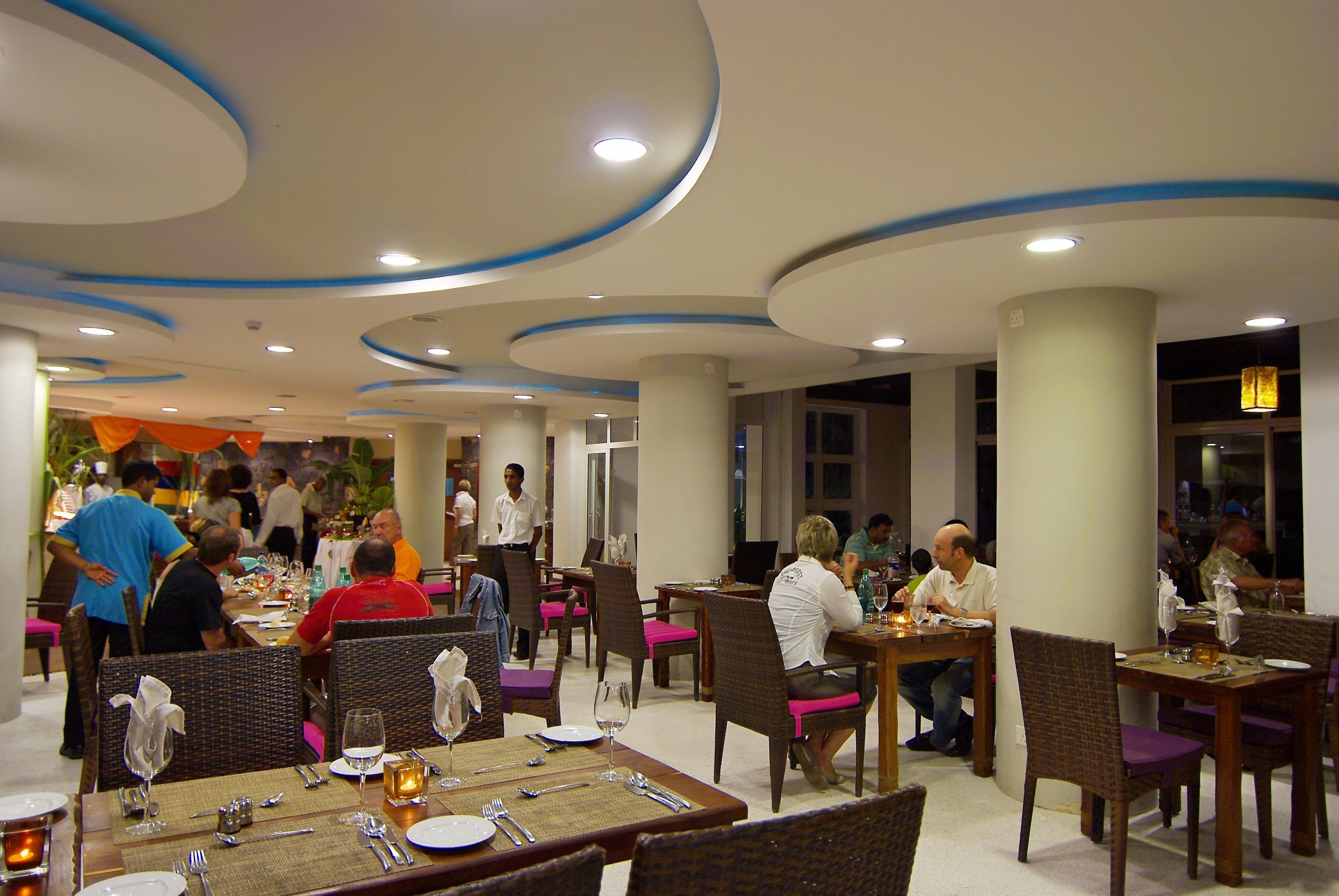 Un restaurante con mesas y sillas redondas, un camarero y comensales.