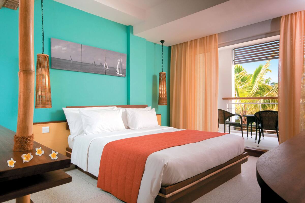 A hotel room with a bed, a dining table, and a balcony with chairs.