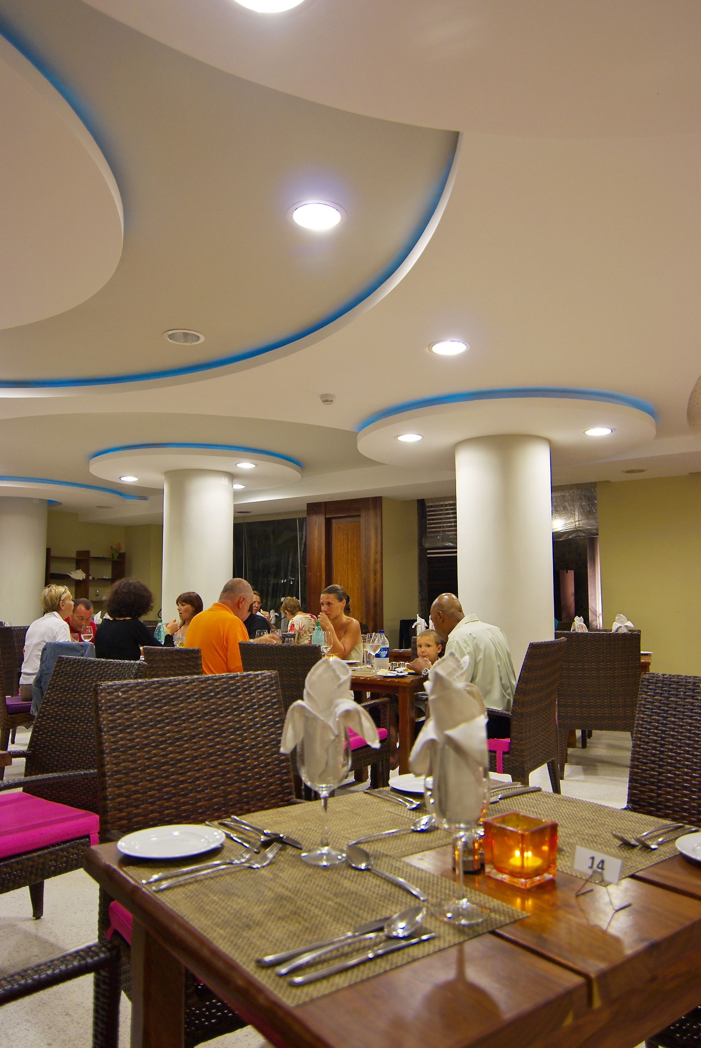 Un espace repas avec des tables rondes, des chaises en osier et un design moderne au niveau du plafond.