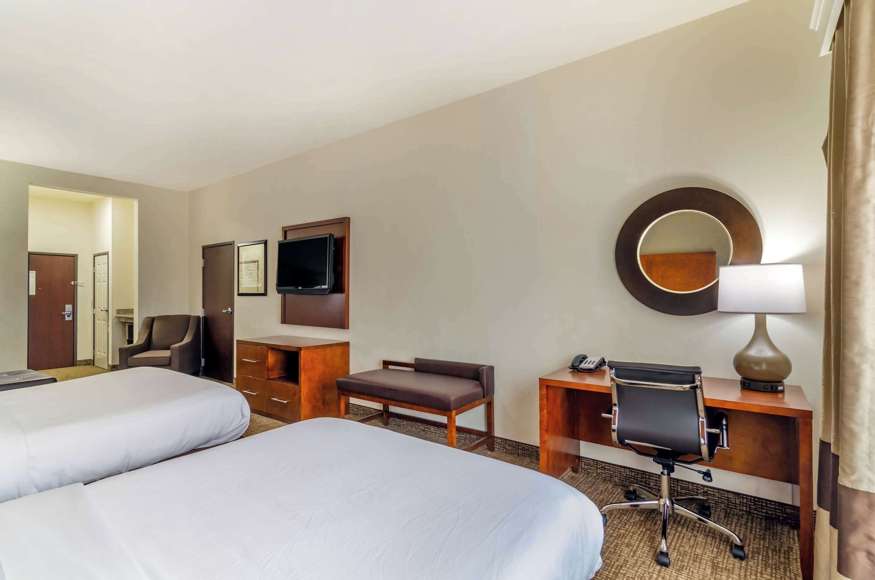 A hotel room with two beds, a desk with a chair, a television, a mirror, and a lamp.