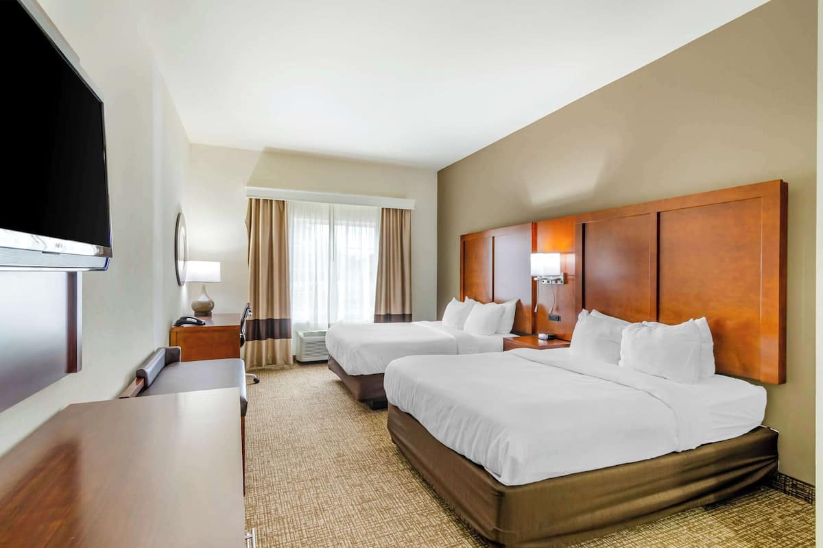A hotel room with two beds, a desk, a TV, and a window with curtains.