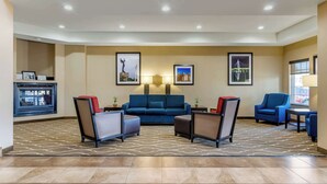 Um saguão de hotel com um sofá azul, duas poltronas, uma mesa pequena e uma tela de televisão.