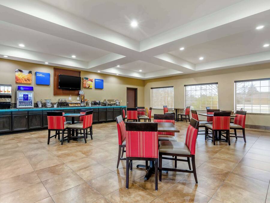 A spacious dining area with multiple tables and chairs, a kitchen counter with a coffee machine, and a television mounted on the wall.