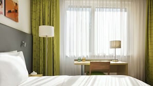 Een hotelkamer met een bed, een bureau, twee lampen en dunne gordijnen.
