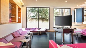 Een moderne woonkamer met een zithoek, een tafelvoetbalspel en een grote televisie.