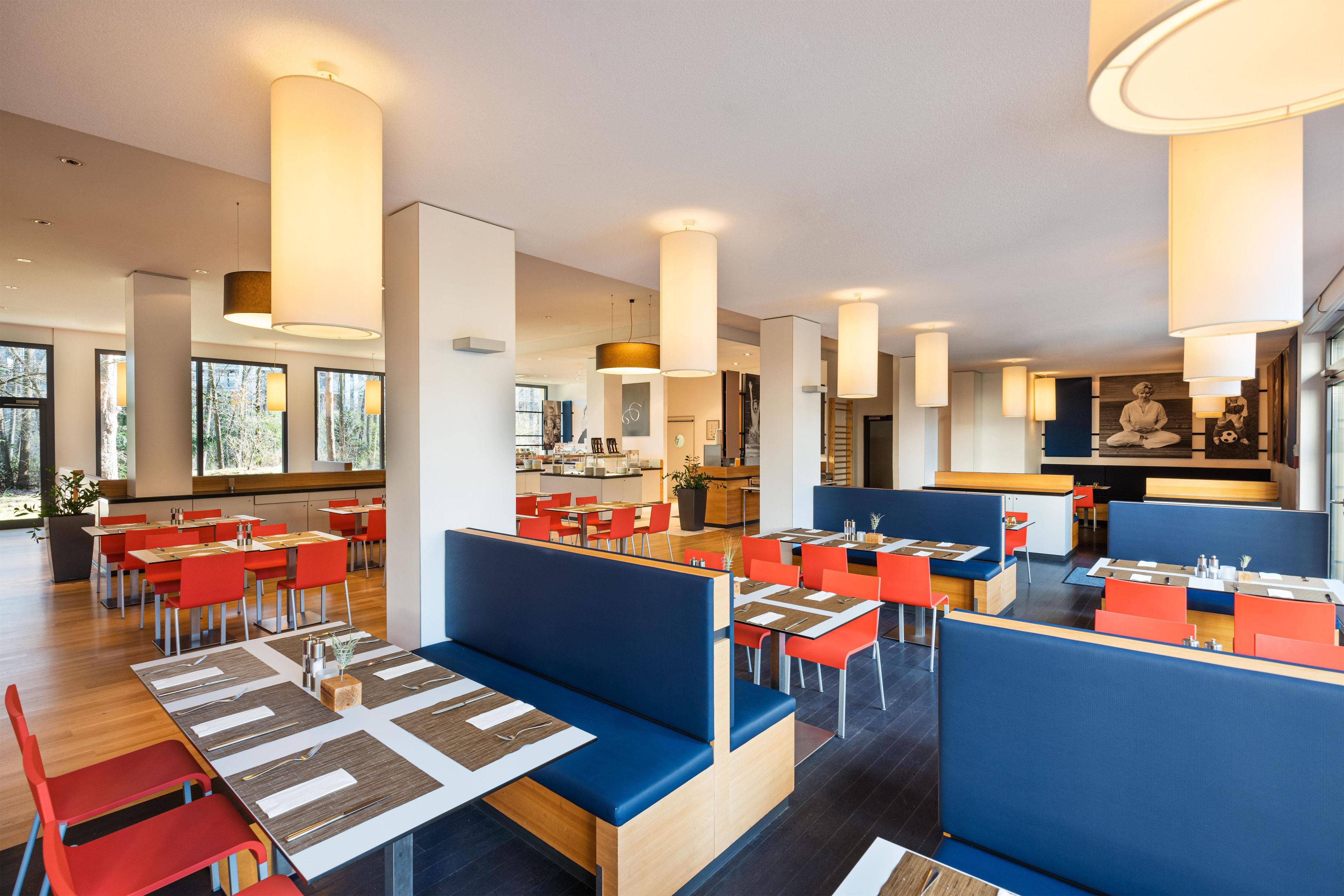 Ein modernes Restaurant mit hohen Decken, Pendelleuchten und einer Mischung aus Sitzecken und Tischen.