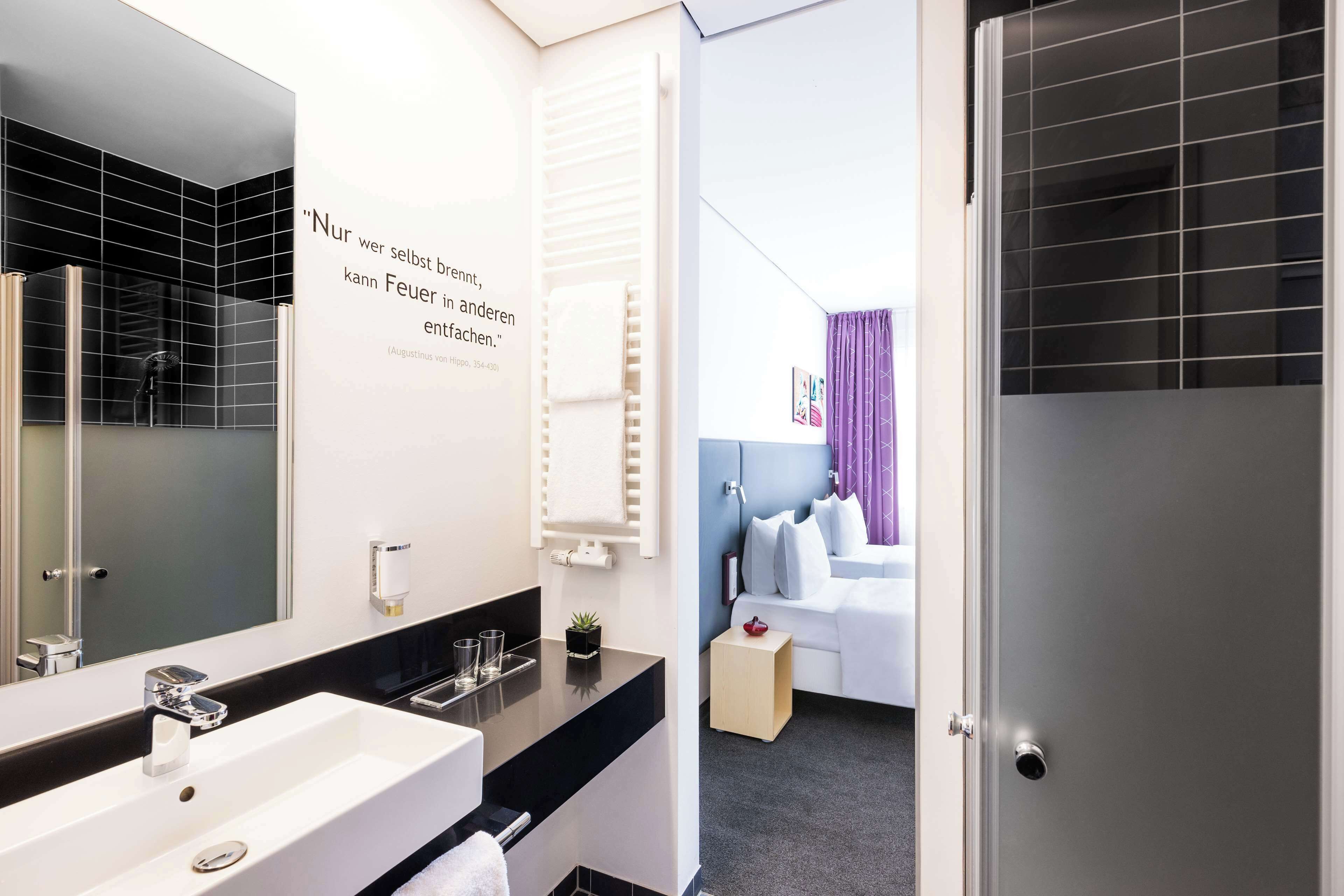 A modern bathroom with a large mirror, a white sink, and a black tiled shower area.