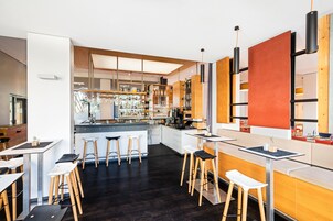 Un área de bar moderna con taburetes, una barra y estantes llenos de botellas y vasos.