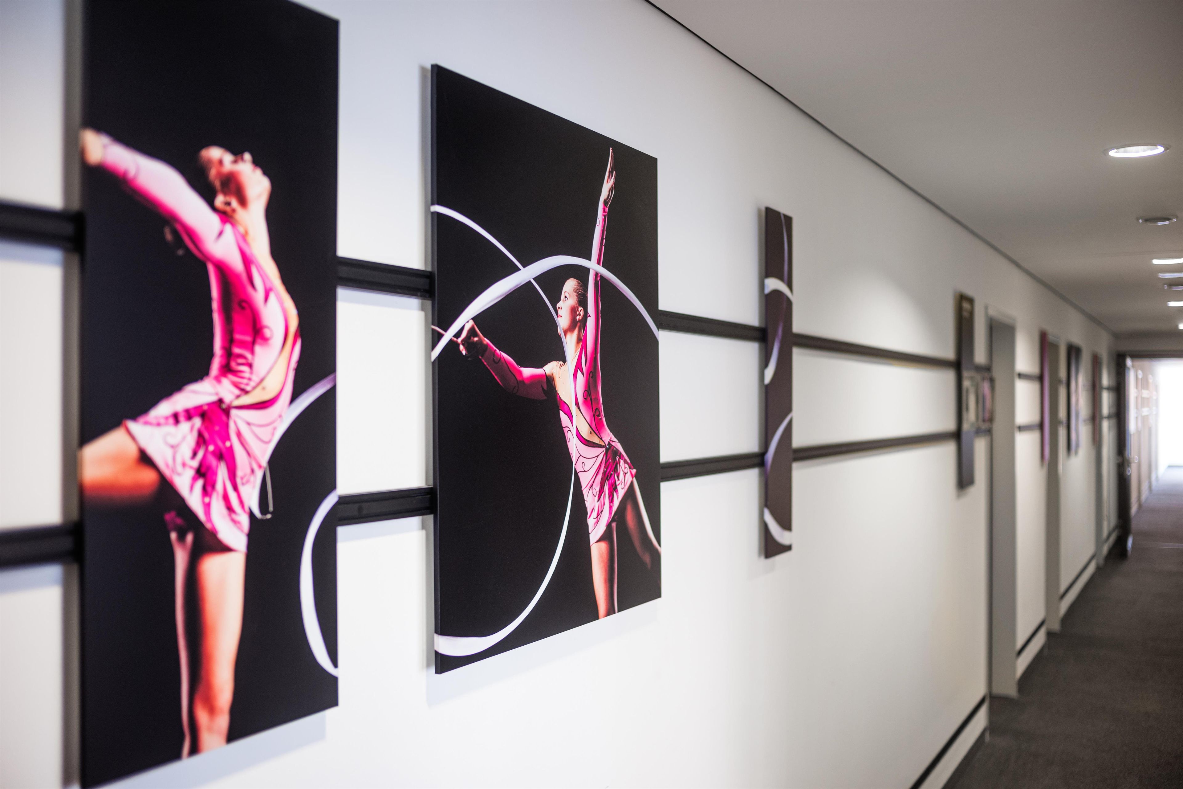 A hallway with framed photographs of a dancer in pink attire, white walls, and a ceiling with recessed lighting.