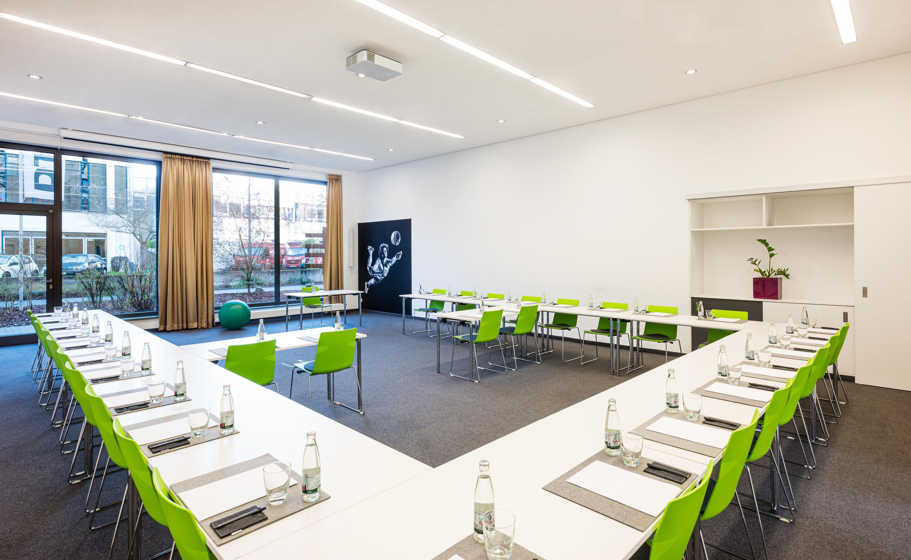 Une salle de conférence équipée de tables et de chaises, de grandes fenêtres et offrant une vue sur l’extérieur.