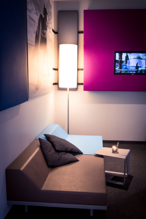Une chambre d’hôtel moderne, dotée d’un canapé, d’une table d’appoint avec une bougie, d’un téléviseur à écran plat fixé au mur et d’un grand tableau encadré.