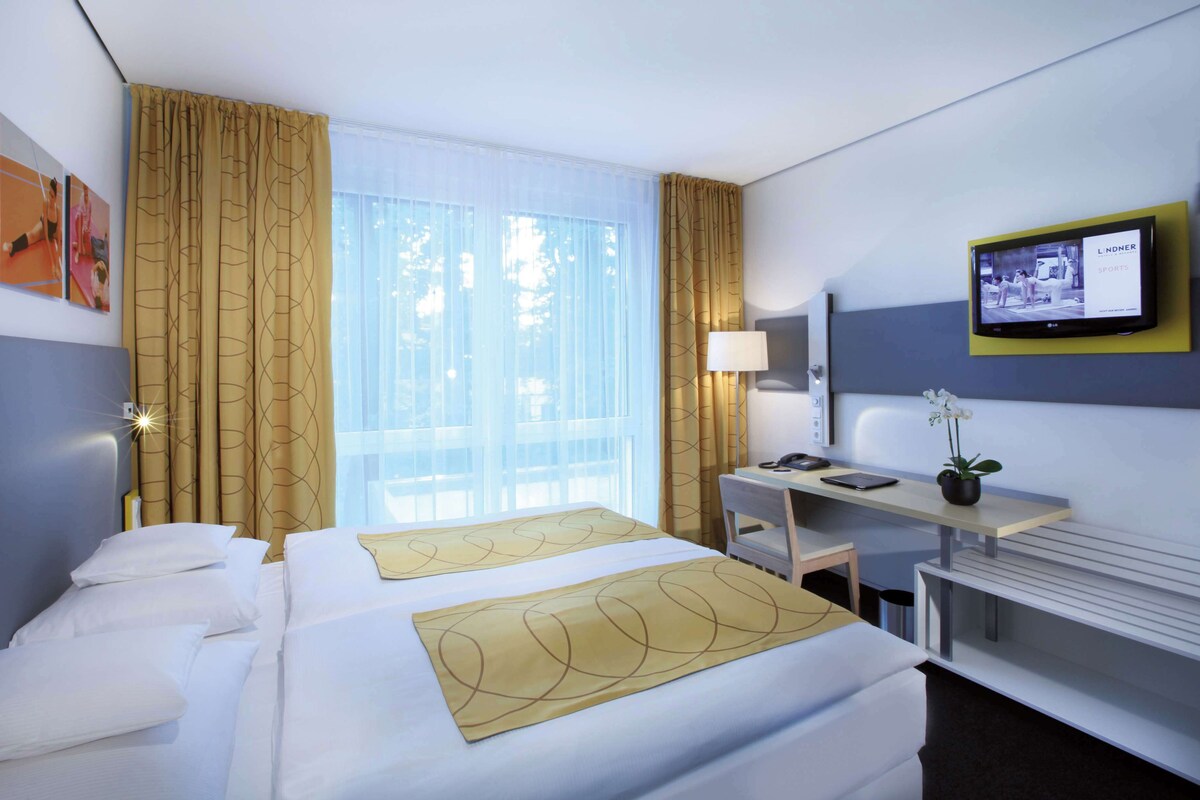 A hotel room with two beds, a desk, a chair, a TV, and a window with curtains.