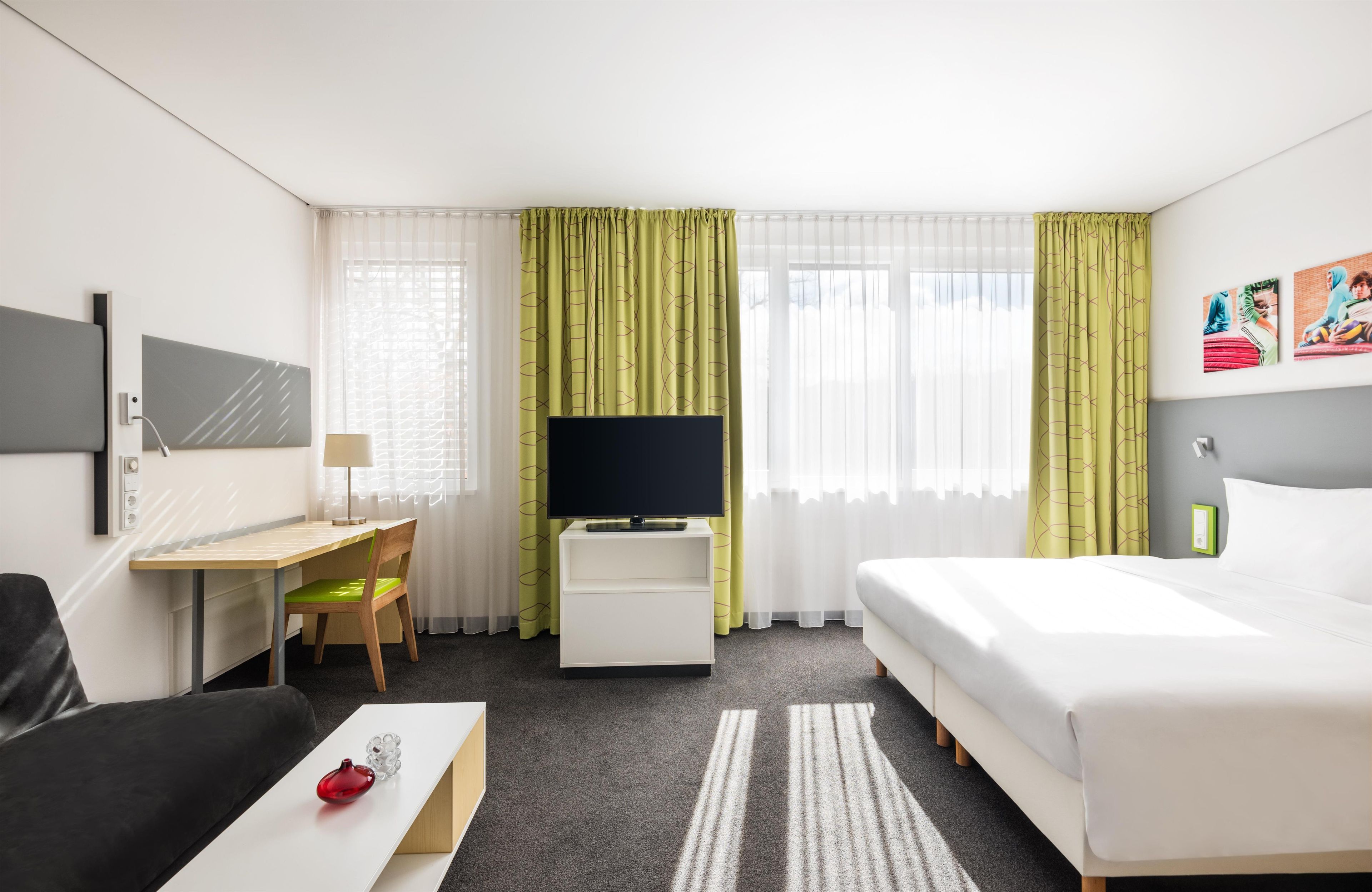 A hotel room with a bed, a desk, a chair, a TV, and a painting on the wall.