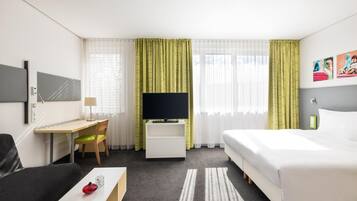 A hotel room with a bed, a desk, a chair, a TV, and a painting on the wall.