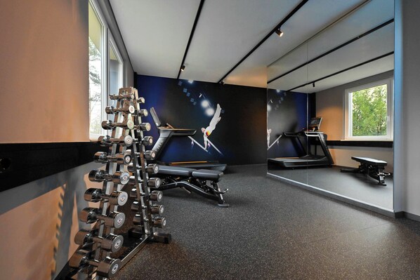A gym with treadmills, a bench press, and a rack of dumbbells. - Lindner Hotel Frankfurt Sportpark, part of JdV by Hyatt (Frankfurt)