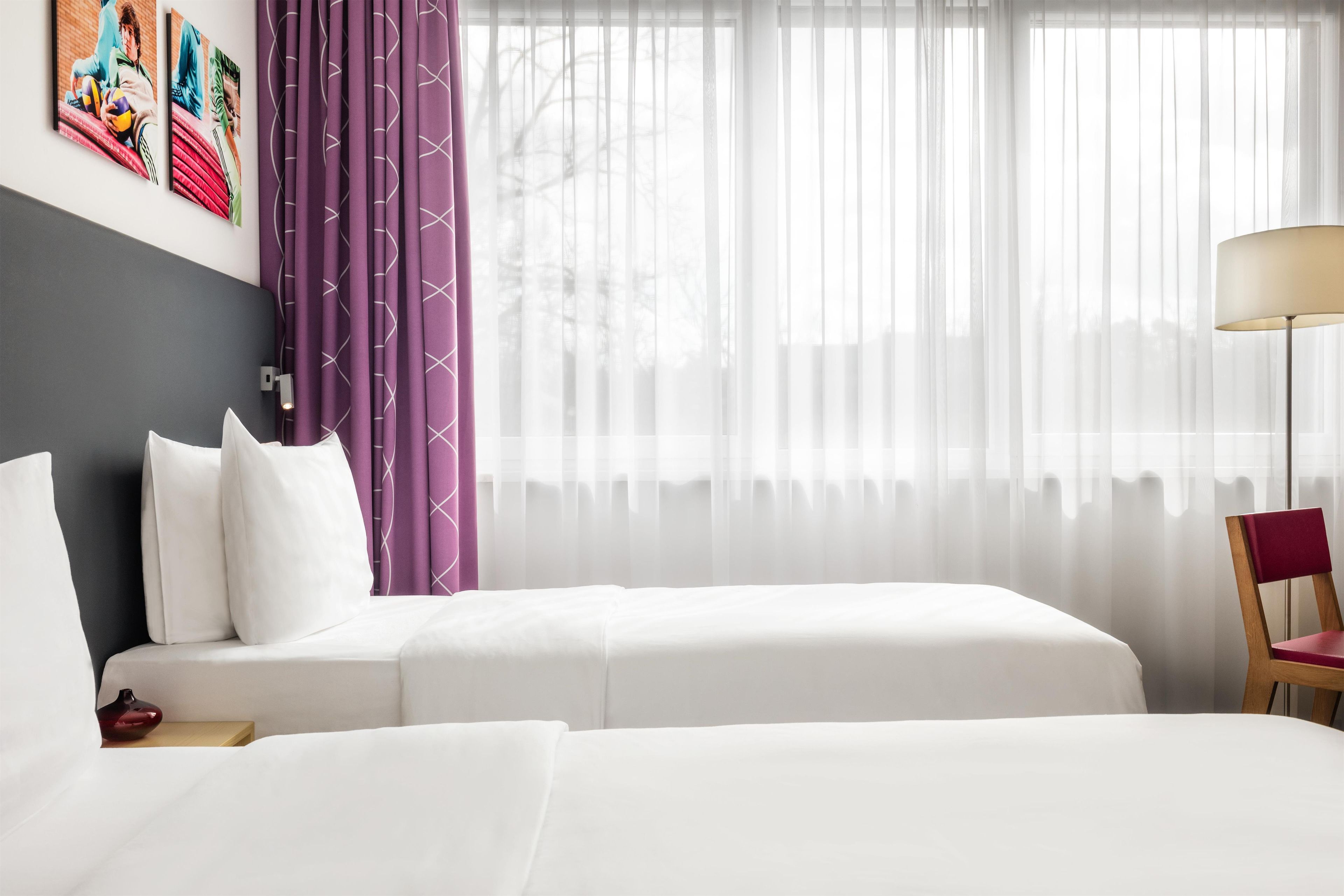 Hotellihuone, jossa on kaksi sänkyä, yöpöytä, lamppu ja tuoli.