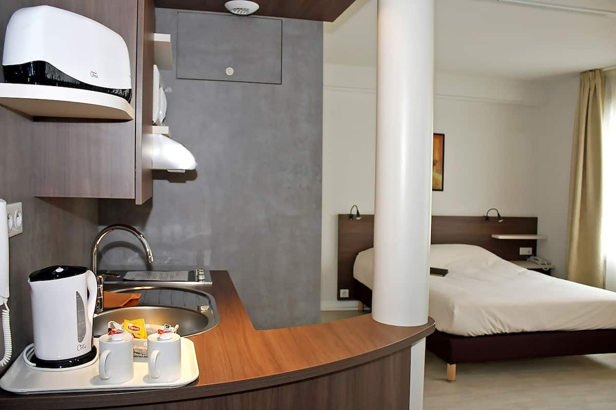 A hotel room with a bed, a bedside table, a lamp, and a bathroom with a sink and a mirror.