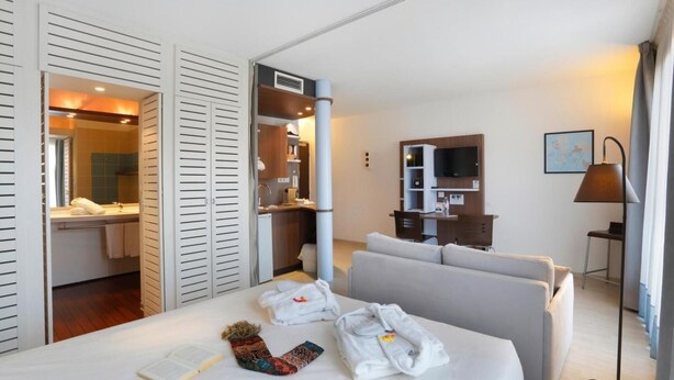 Habitación de hotel con cama, escritorio, televisor y baño visible a través de una puerta corredera.