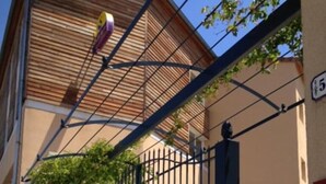 Una entrada protegida por un portón metálico, una pérgola de madera y un letrero con el número 5.