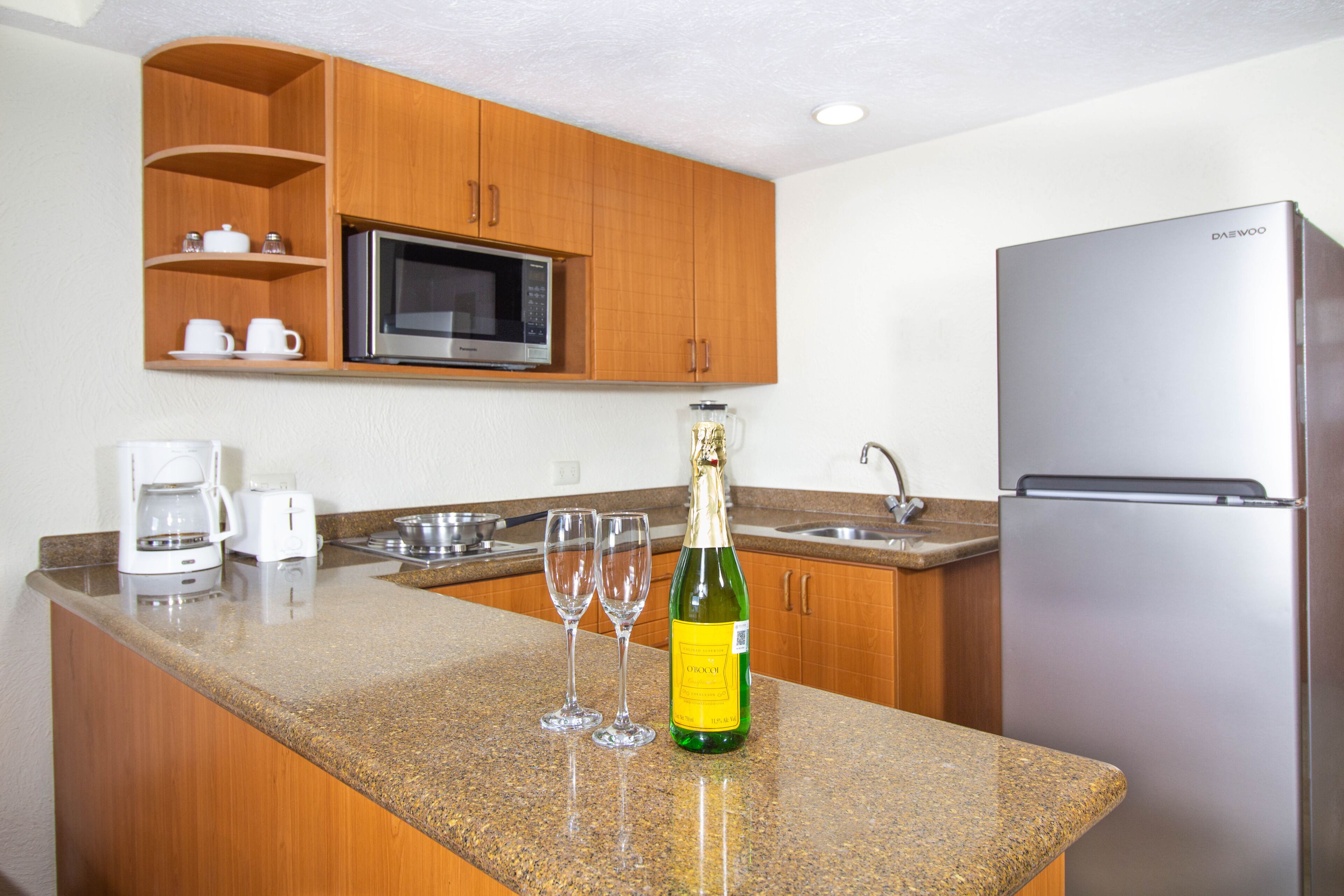Una cocina con armarios de madera, un refrigerador de acero inoxidable, un microondas y una botella de champán sobre la encimera.